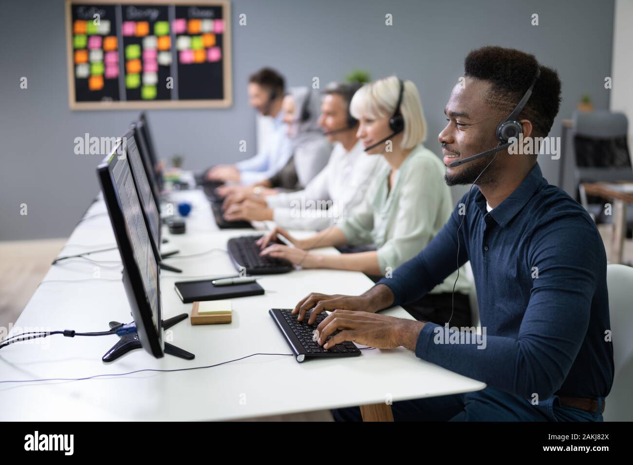 L'agent des services à la clientèle masculine positive avec casque de travail dans un centre d'appels Banque D'Images