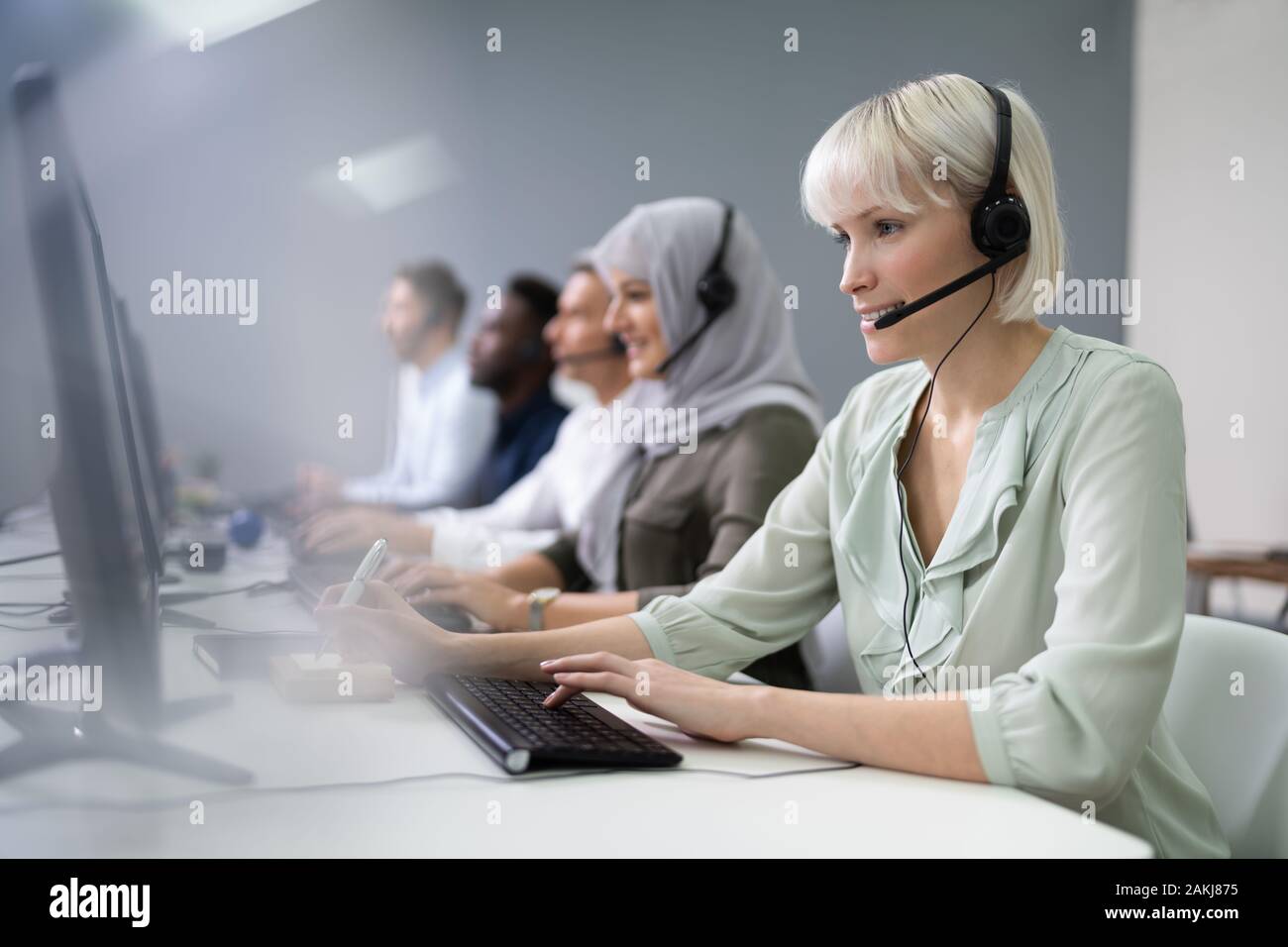 L'agent des services à la clientèle féminine positive avec casque de travail dans un centre d'appels Banque D'Images