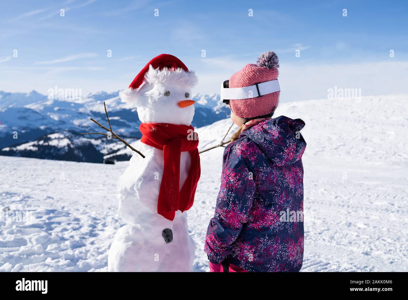 Little Girl standing in front of Snowman avec écharpe rouge et Christmas Hat Banque D'Images