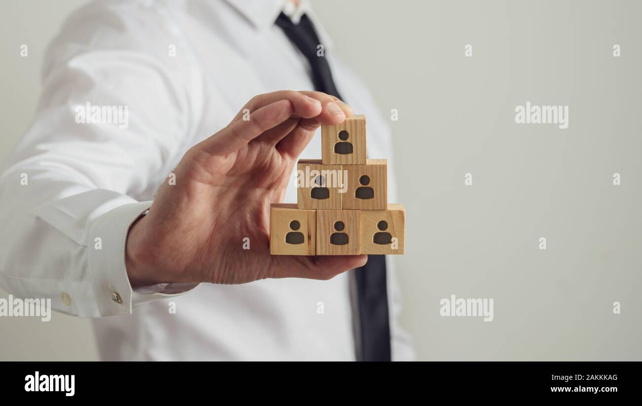 Business executive holding cubes en bois avec icône personne sur eux construire dans une structure pyramidale. Image conceptuelle de l'emploi et des ressources humaines. Banque D'Images
