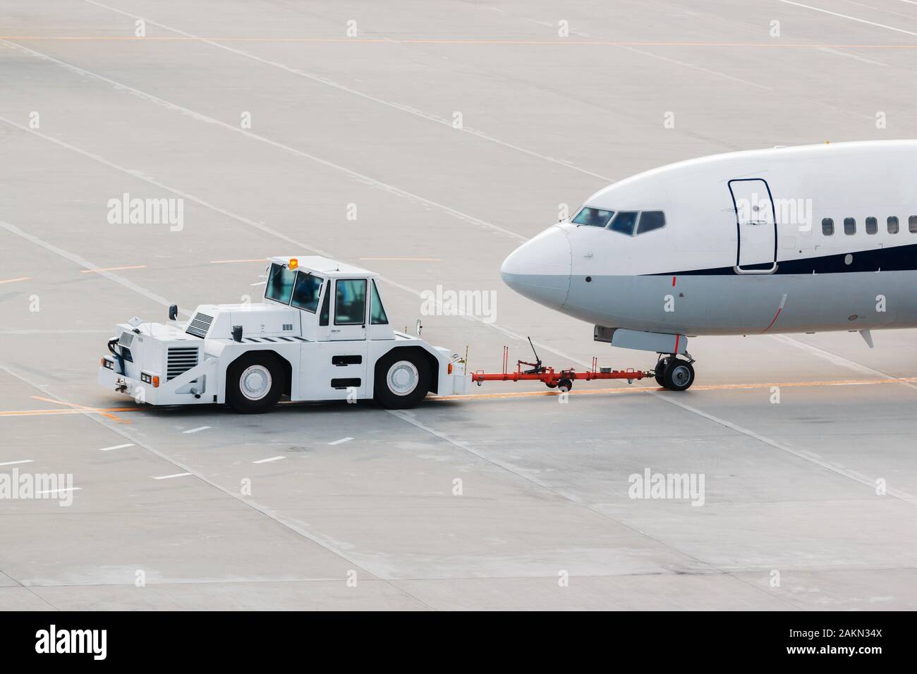 Avion sur la piste de l'aéroport avec pushback tracteur attelé à l'avion train avant le remorquage par véhicule terrestre à la borne d'embarquement. Banque D'Images