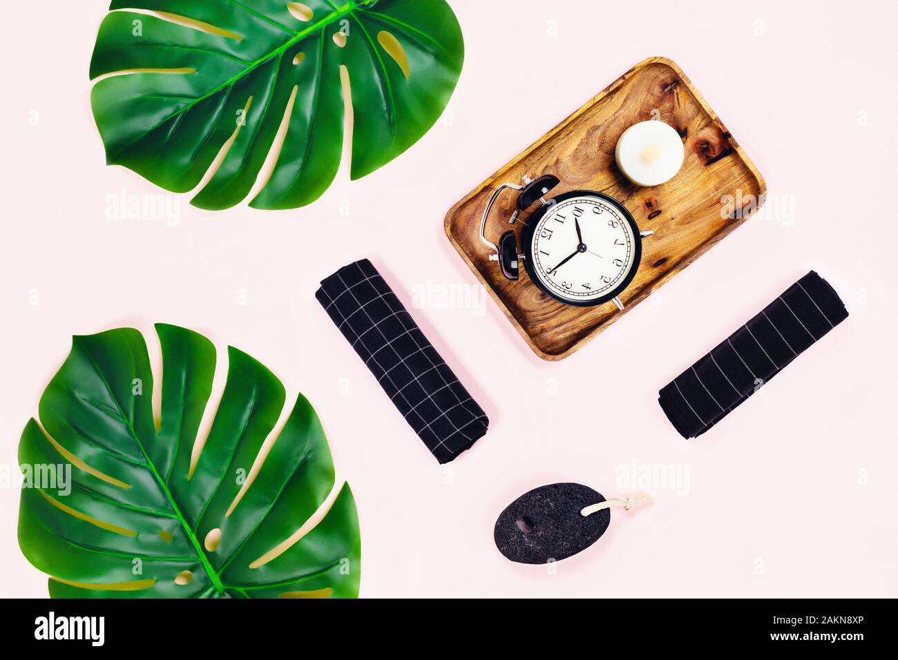 Plateau en bois avec fond rose et noir réveil avec pierre ponce entouré de feuilles tropicales. Mise à plat, vue du dessus. Concept Spa. Banque D'Images