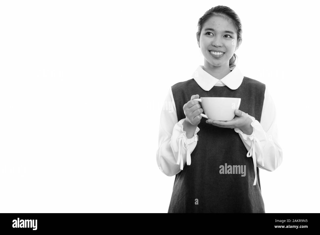 Studio tourné de jeune femme asiatique heureuse souriant et tenant une tasse de café tout en pensant Banque D'Images