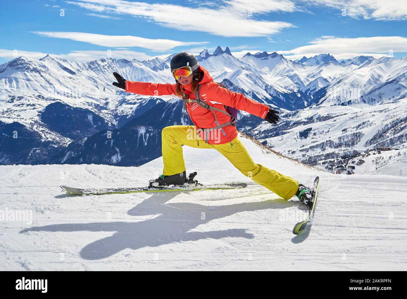 Femme skieur s'étendant sur les skis avec une pose drôle, haut au-dessus sur une piste de ski dans le domaine skiable des Sybelles, France, sur une journée d'hiver ensoleillée, avec les Aigeuil Banque D'Images
