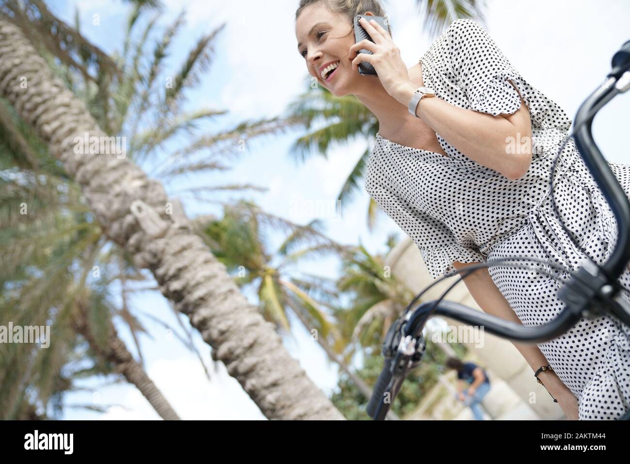 Pretty young woman sitting on bicycle outdoors talking on cellphone Banque D'Images