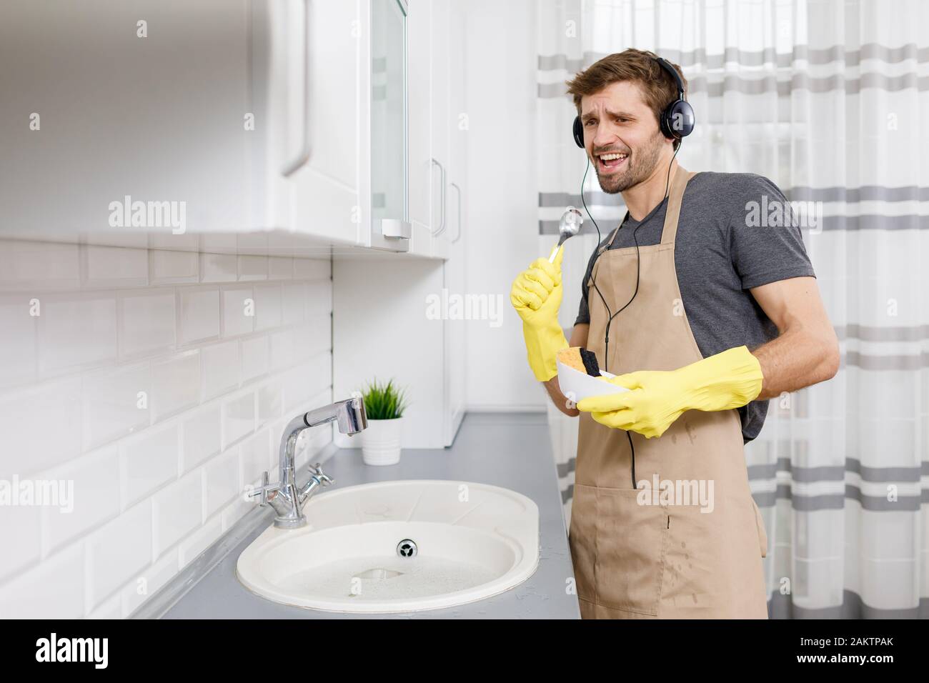 Jeune homme dans un casque chantant avec une cuillère comme un microphone pendant le lavage de la vaisselle Banque D'Images