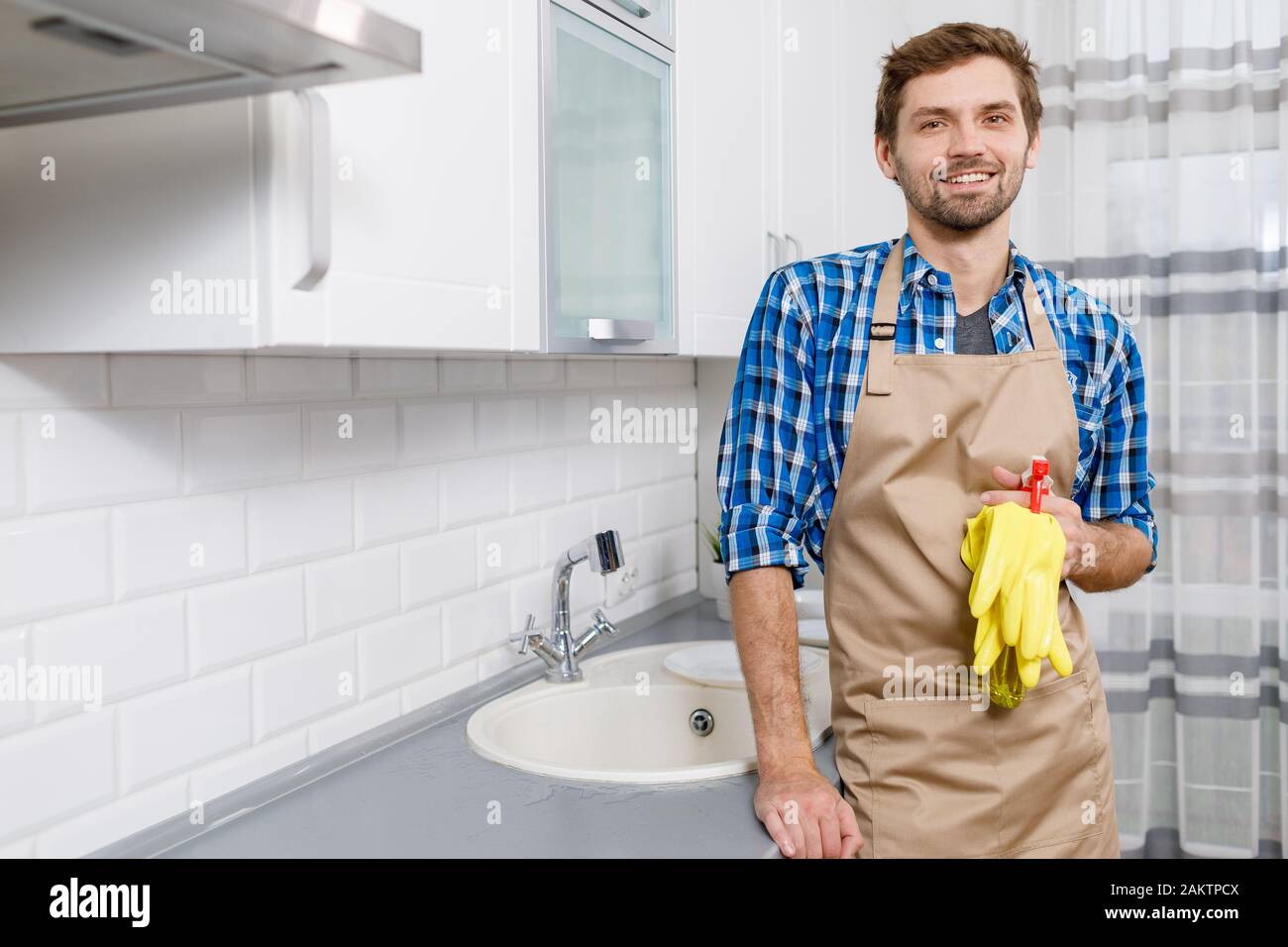 Jeune homme de handsome en tablier se posant avec des gants et nettoyer à mesure que le ménage est fini Banque D'Images