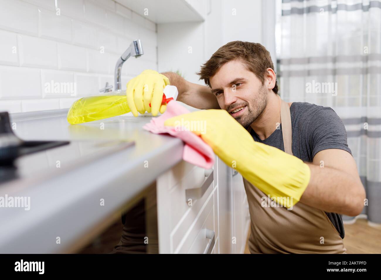 Gros plan de jeune homme dans des gants jaunes à l'aide d'un nettoyant pour laver les meubles de cuisine Banque D'Images
