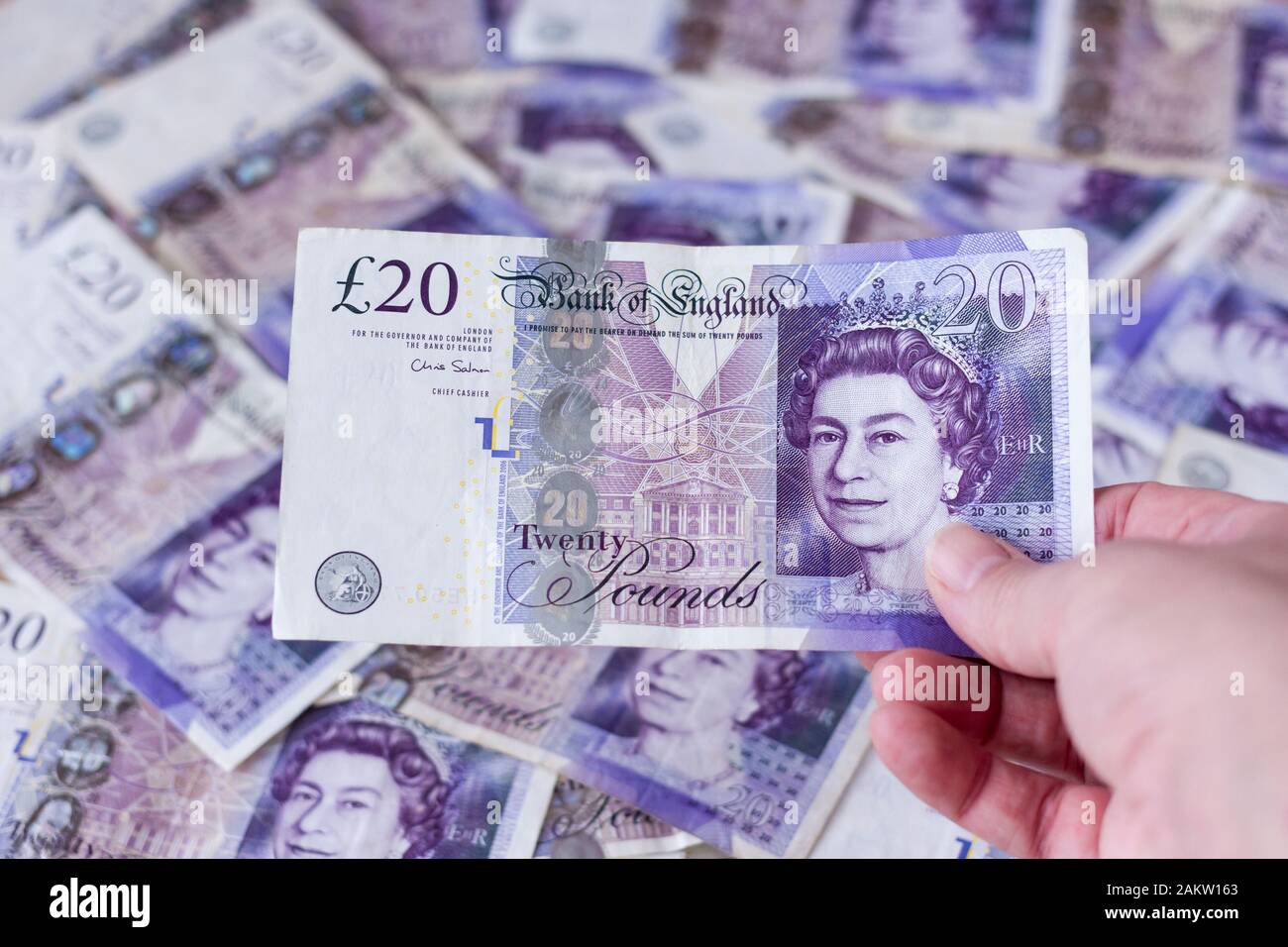 Détenir une note britannique de vingt livres sterling avec plus de notes en arrière-plan Banque D'Images
