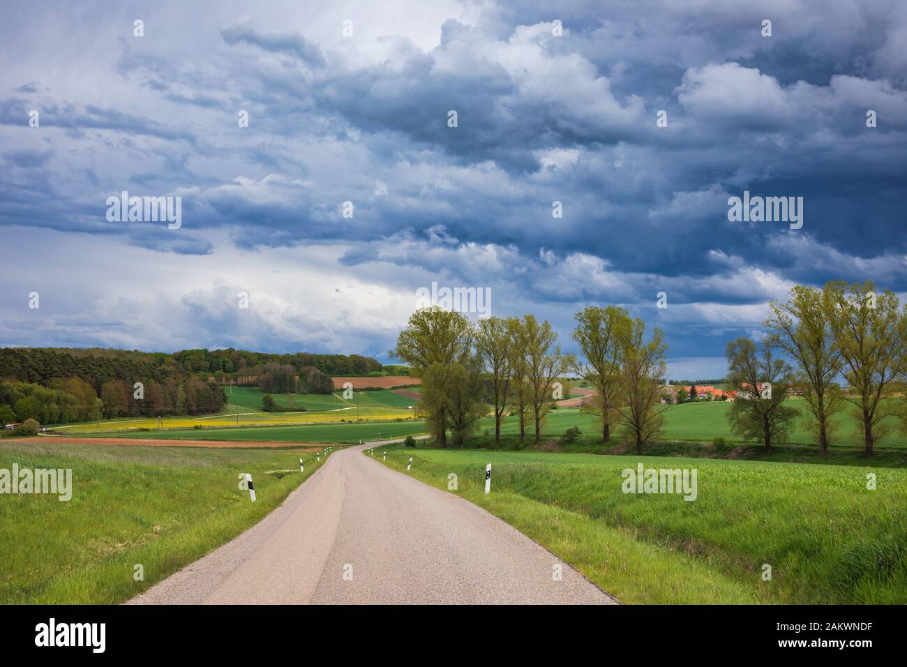 Spectaculaire ciel orageux sur route d'asphalte serpentant à travers les champs verts en Bavière rurale, Allemagne Banque D'Images