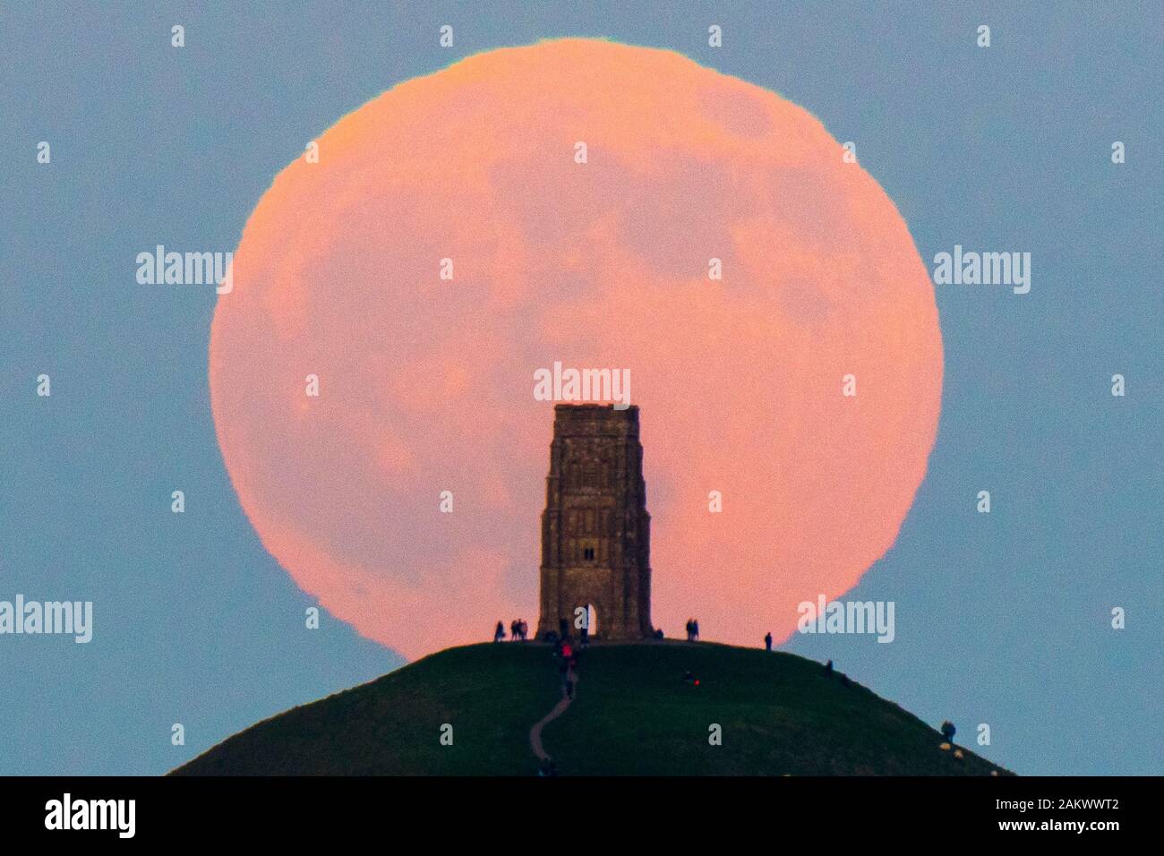 Glastonbury, Somerset, Royaume-Uni. 10 janvier 2020. Météo britannique. Le loup pleine lune se lève derrière Tor de Glastonbury dans le Somerset sur une bonne soirée d'hiver où les visiteurs se sont réunis pour regarder le lever de la lune au coucher du soleil. Crédit photo : Graham Hunt/Alamy Live News Banque D'Images