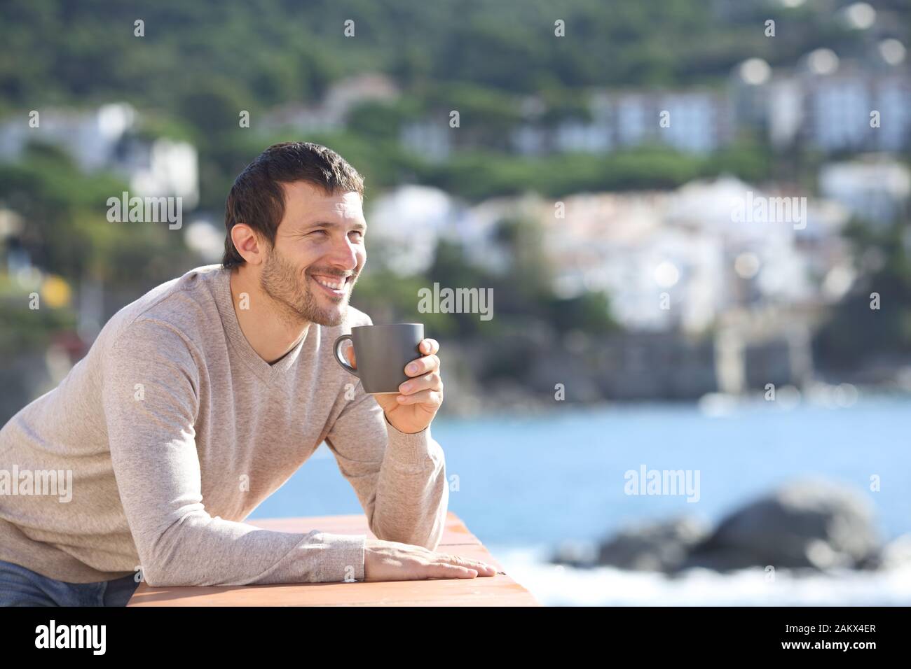 Homme heureux de boire du café en contemplant une vue en balcon sur la plage d'une journée ensoleillée Banque D'Images