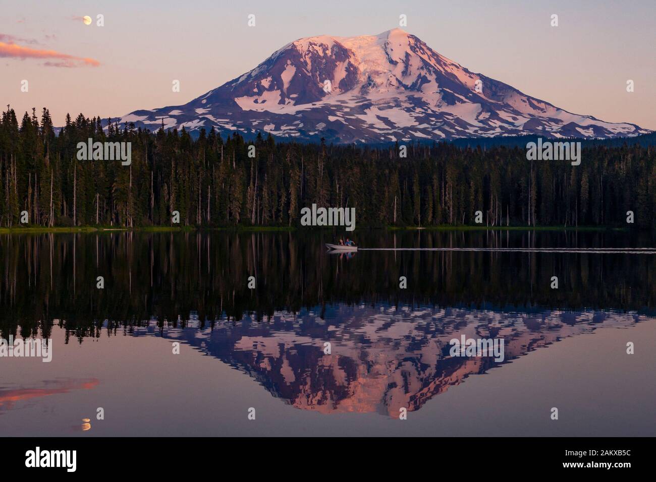 La lune s'élève sur le mont Adams et une réflexion est vue dans le paisible lac de Takhlakh au coucher du soleil. Les plaisanciers en famille apprécient le temps de l'été au loin. Banque D'Images