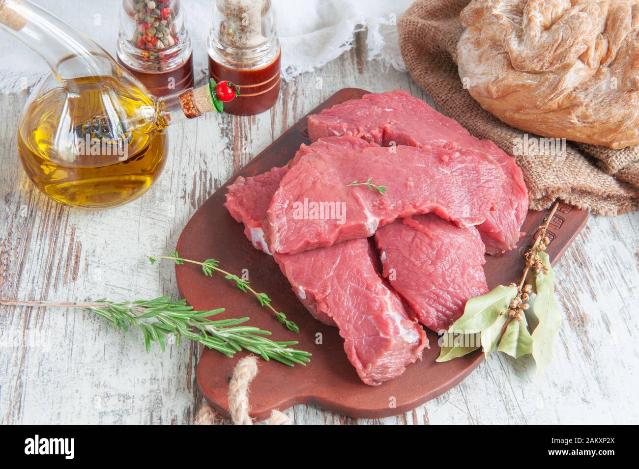 Des morceaux de viande sont prêts pour la marinade se trouvent sur un panneau d'argile avec des épices-Bay feuille, poivre, herbes provençales. Banque D'Images