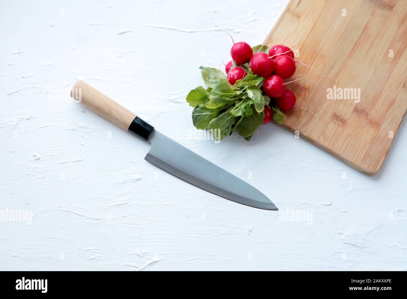 Radis frais et grand couteau de cuisine sur fond blanc et vieux tableau de découpe en bois. Espace de copie Banque D'Images