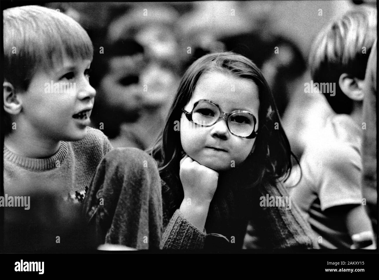 Très vraie petite fille intentante regardant les autres pendant l'assemblage à l'école pour les élèves de première classe en noir et blanc du film Banque D'Images