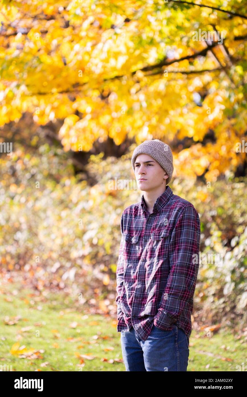 Jeune garçon pensif en toque et chemise en flanelle devant des arbres jaunes Banque D'Images