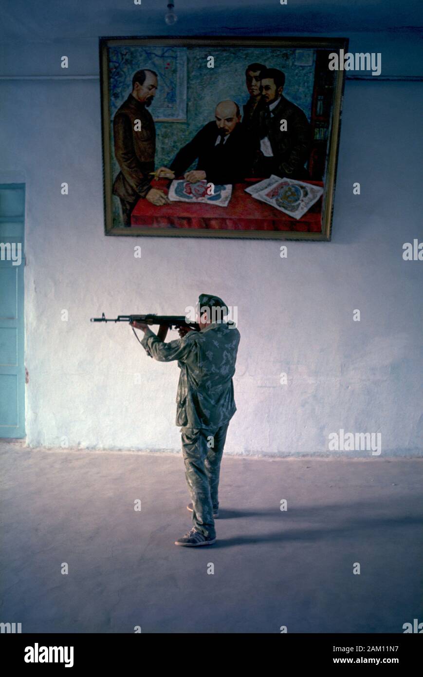 Le Tadjikistan au soldat de l'une des entrées de la Base de patrouille à la frontière de la CEI à Pyandzh, au Tadjikistan. Un pointage est celui du soldat kalachnikov à la base porte et permanent, sous une vieille peinture soviétique Vladimir Lénine montre que Feliks Dzierzynski et et d'autres bolcheviks à une table. Banque D'Images