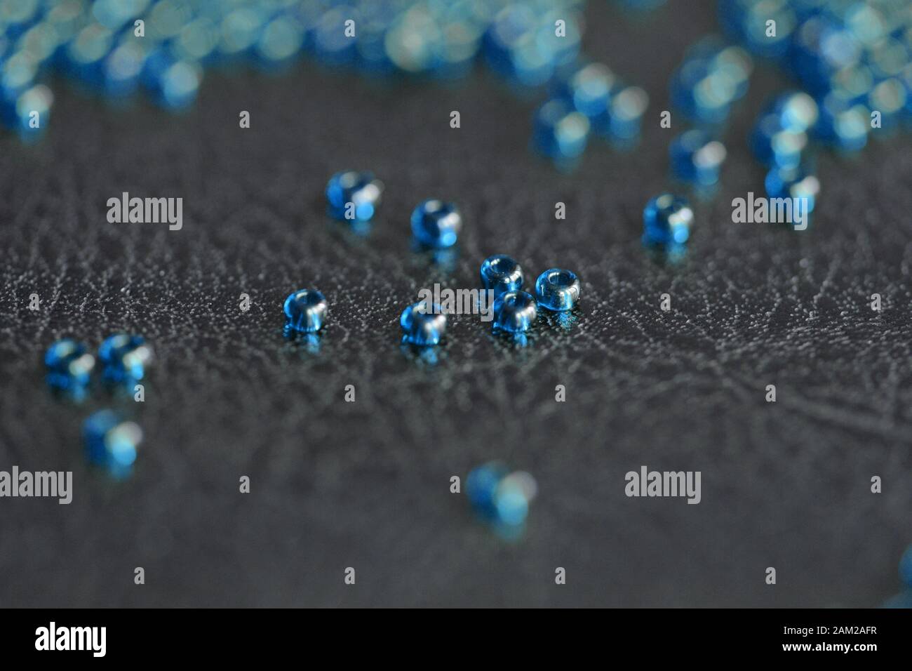 Perles de semences transparentes couleur bleue diffusée sur une surface en cuir noir de gros plan Banque D'Images