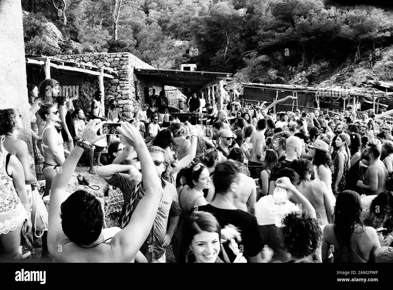 Noir et blanc des foules dansant sur Hippy Beach Ibiza, Ibiza, Cala Beniras Beach Drummers sur la gauche de l'image Banque D'Images