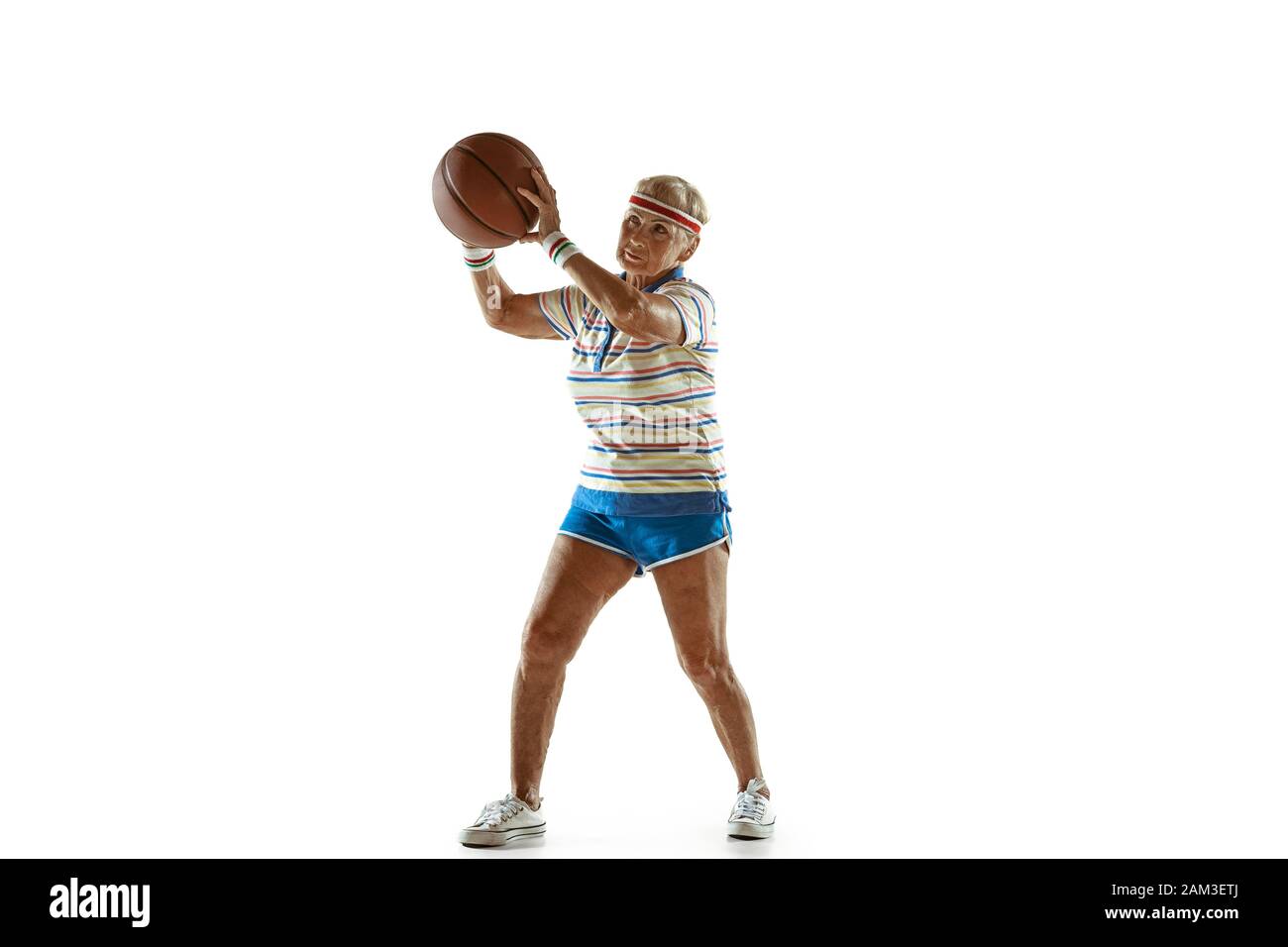 Se déplacer. Senior woman wearing sportwear jouer au basket-ball sur fond blanc. Portrait modèle féminin en grande forme reste actif. Concept de sport, activité, mouvement, bien-être, la confiance. Copyspace. Banque D'Images