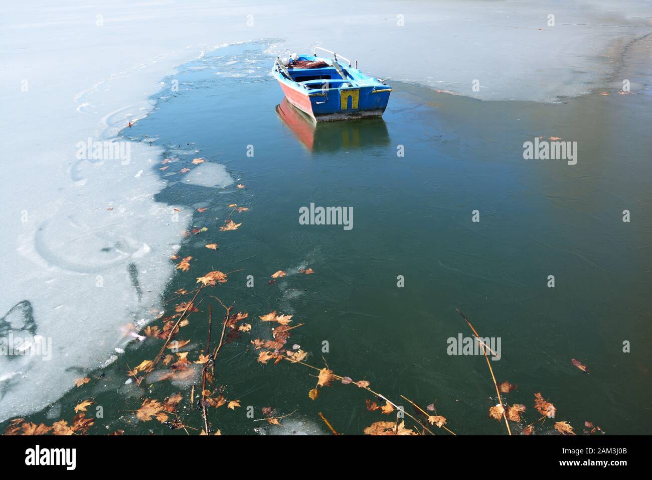 Feuilles d'arbre d'avion et bateau de pêche piégés dans l'eau glacée du lac Orestiada à Kastoria, Grèce Banque D'Images