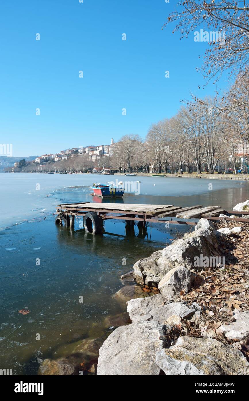 Bateau dans le lac gelé Orestiada, ancien quai en bois et Kastoria ville comme arrière-plan Banque D'Images