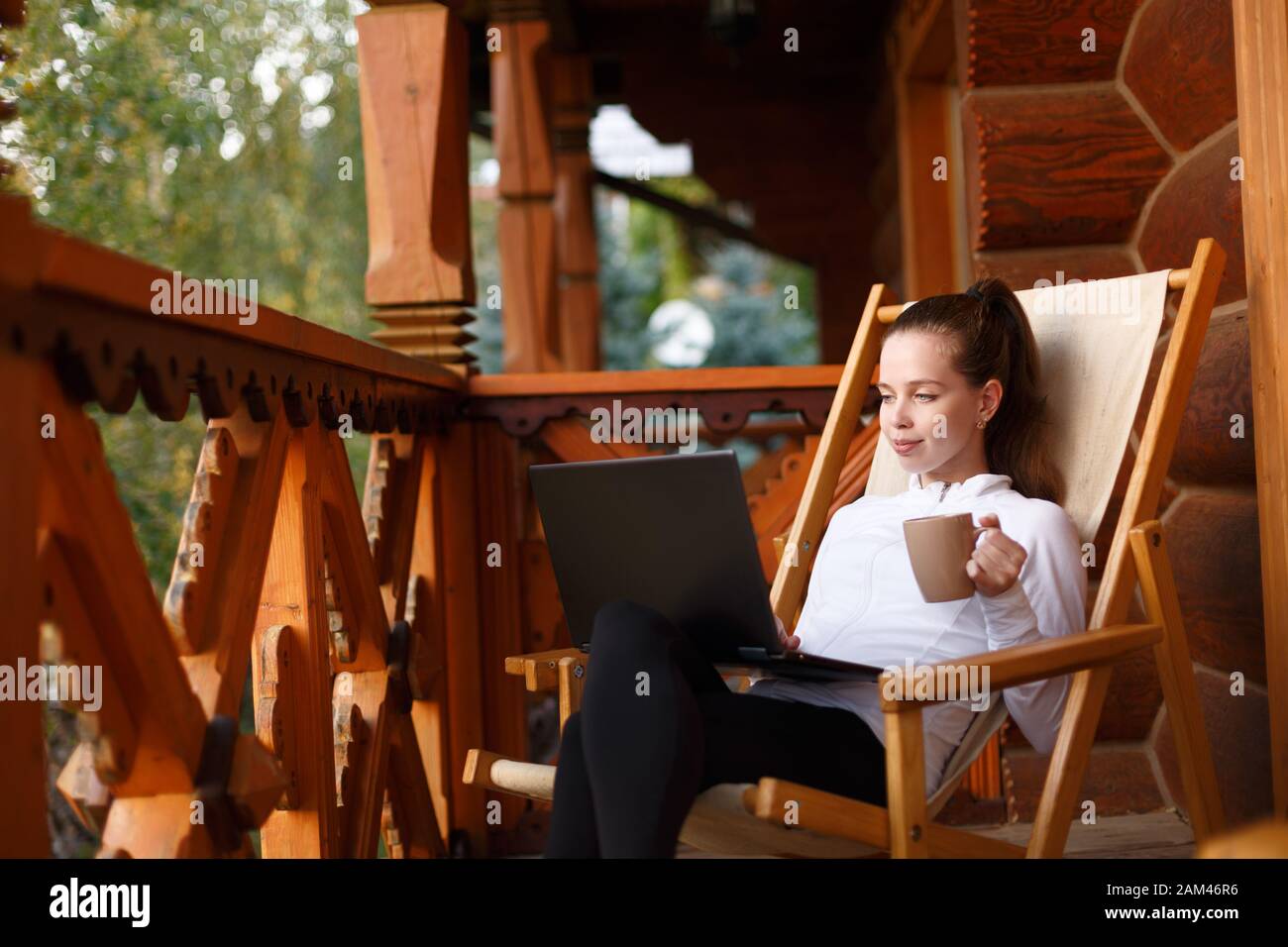 Une jeune femme d'affaires séduisante travaille sur l'ordinateur portable de la station de montagne avec une tasse de thé et de cookie. La femme se détend sur une chaise longue avec ordinateur portable Banque D'Images