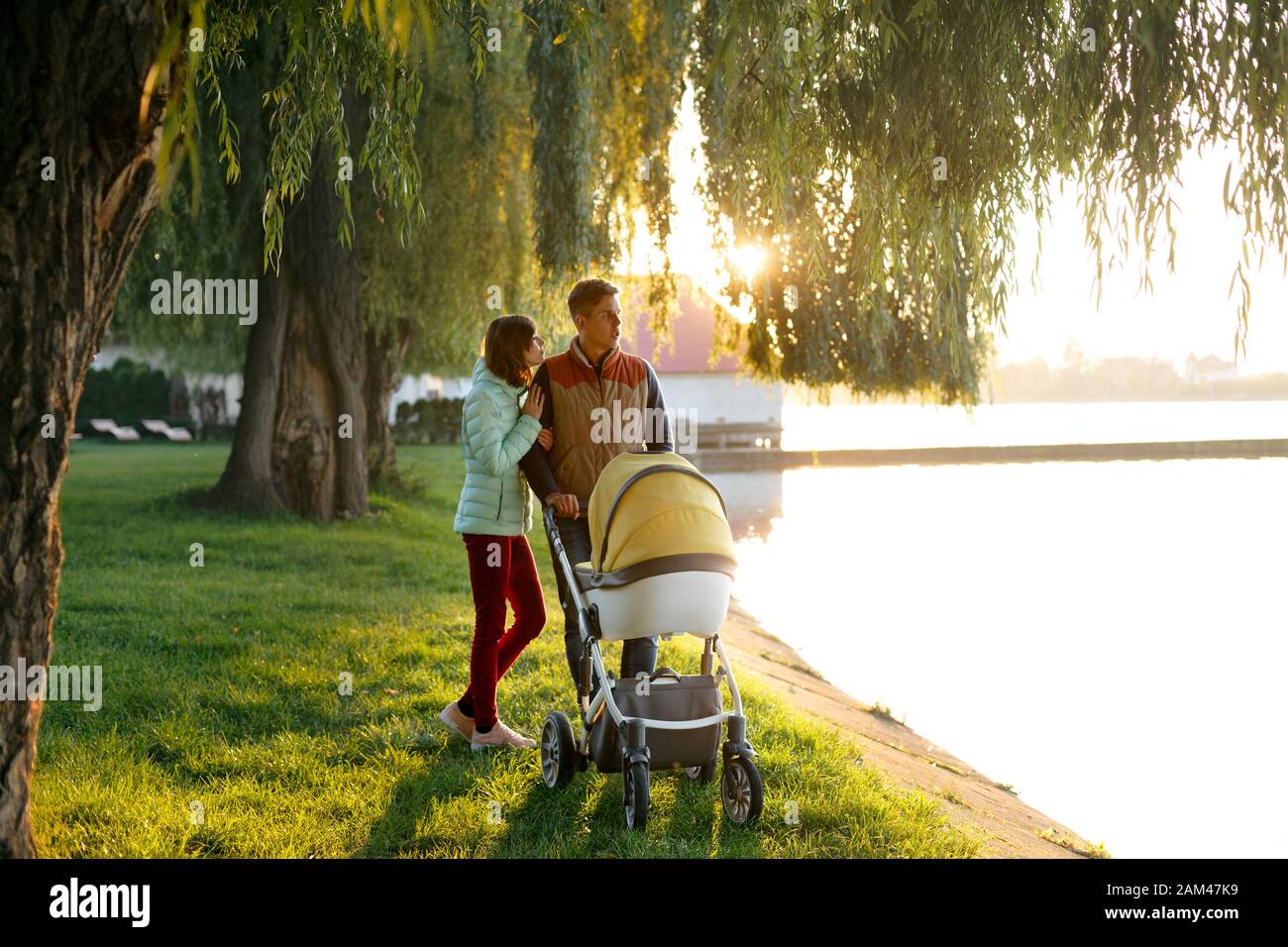 Une Jeune Famille Affectueuse Marche Pres Du Lac Avec Une Poussette Couple De Parents Souriants Avec Bebe Bebe Dans Le Parc D Automne L Amour La Parentalite La Famille La Saison Et Photo Stock