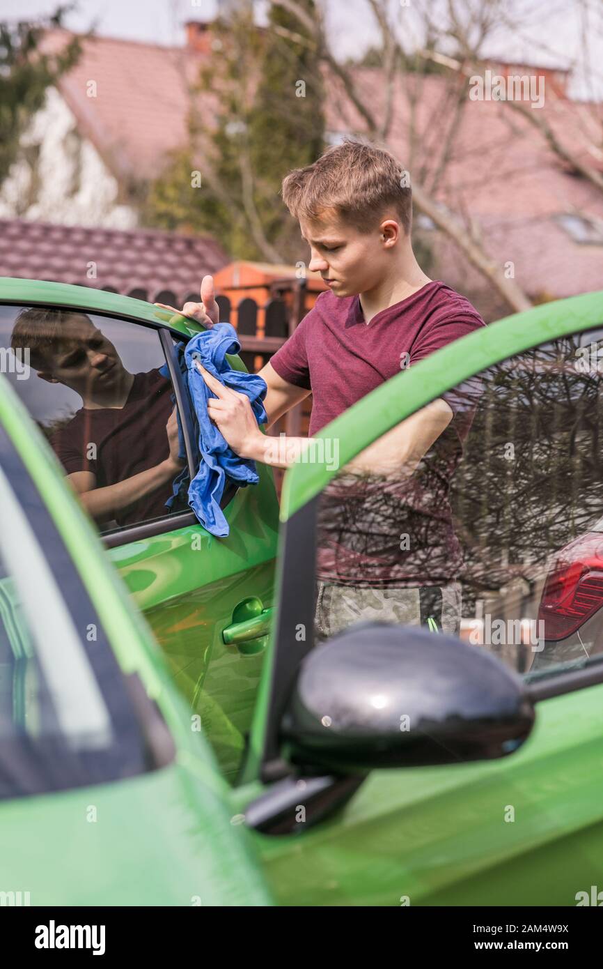 Le nettoyage de printemps. Jeune garçon est la voiture verte de polissage. Banque D'Images