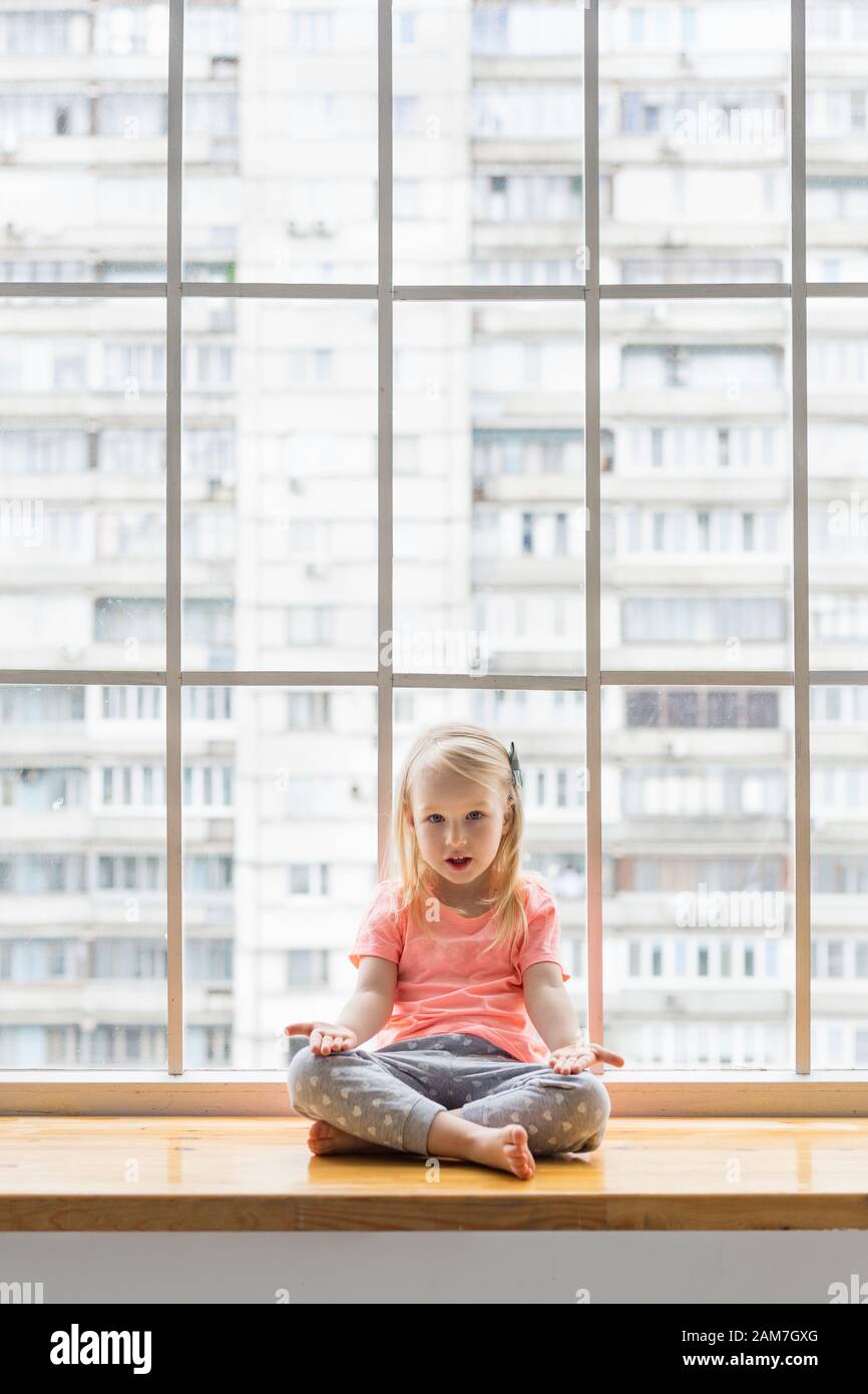 fille de 3 ans assise dans lotus pose asana avec des jambes croisées devant la fenêtre Banque D'Images