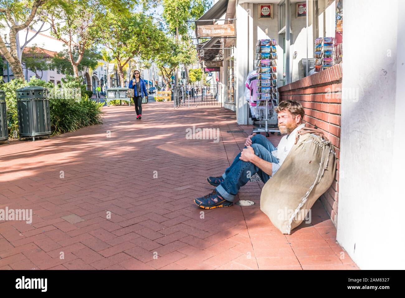 Une trentaine de sans-abri barbu homme assis et la mendicité tout en appuyé contre une devanture avec son bundle maintenant ses effets personnels à côté de lui. Banque D'Images