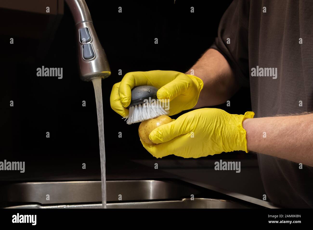 Gros plan sur le lavage et le rinçage des pommes de terre en préparation à la cuisson. Modèle avec gants en caoutchouc jaune jetables. Banque D'Images