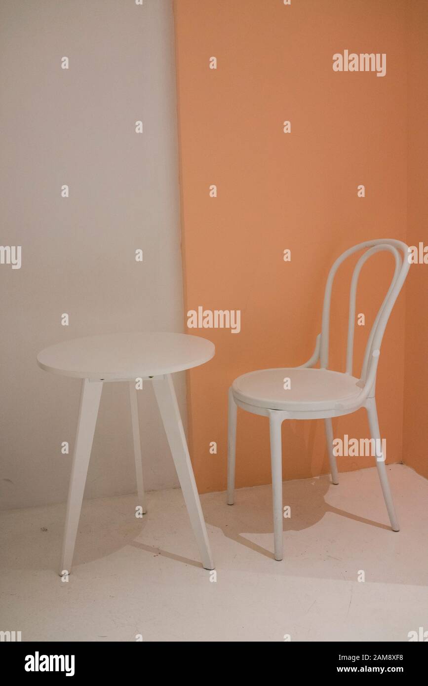 Chaise blanche confortable et petite table blanche avec mur blanc et orange clair à l'arrière-plan. Banque D'Images