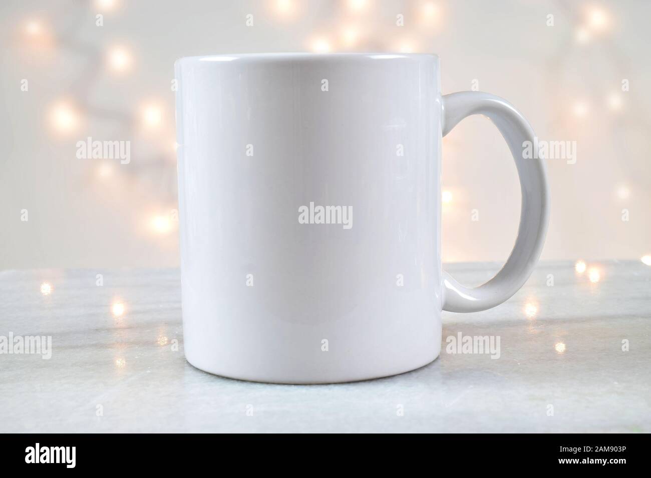 Une tasse à café de 11 oz repose délicieusement sur un fond de marbre avec des lumières de Noël blanches illuminant à l'arrière-plan. Ajoutez votre propre motif au mug. Banque D'Images