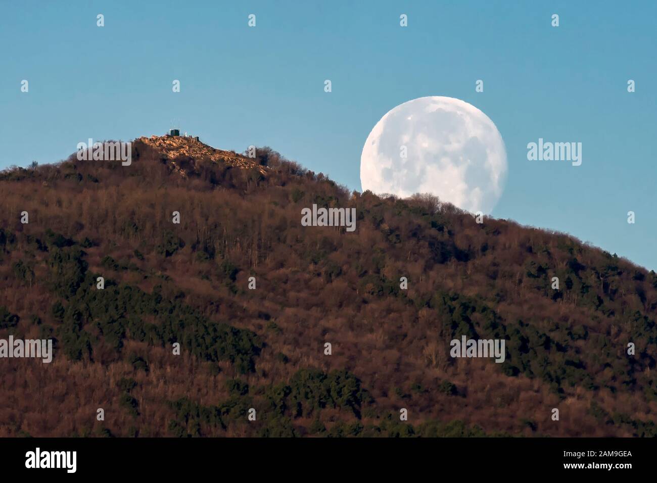 La pleine lune se fixe tôt le matin derrière une montagne contre le ciel bleu Banque D'Images