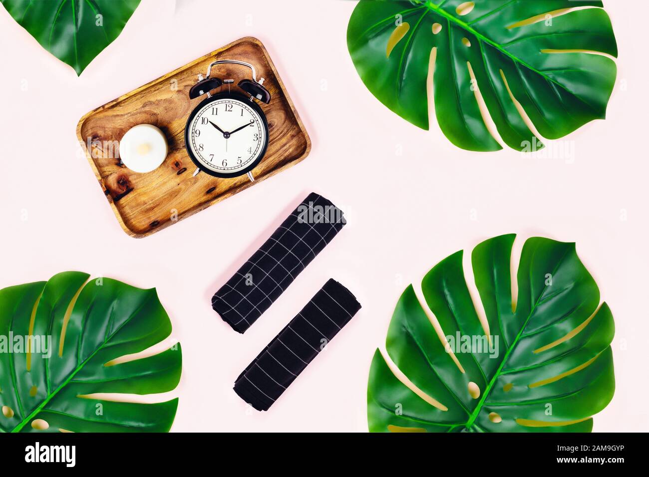 Fond rose avec plateau en bois et réveil noir, pierre ponce entourée de feuilles tropicales. Plat, vue du dessus. Concept de spa. Banque D'Images