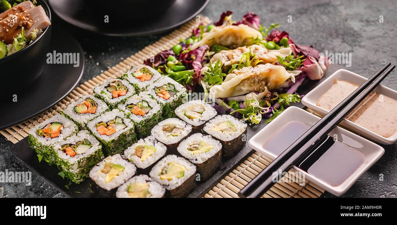Bannière de nourriture asiatique. Gros rouleaux de sushi avec légumes et boulettes. Cuisine chinoise sur fond gris en béton Banque D'Images