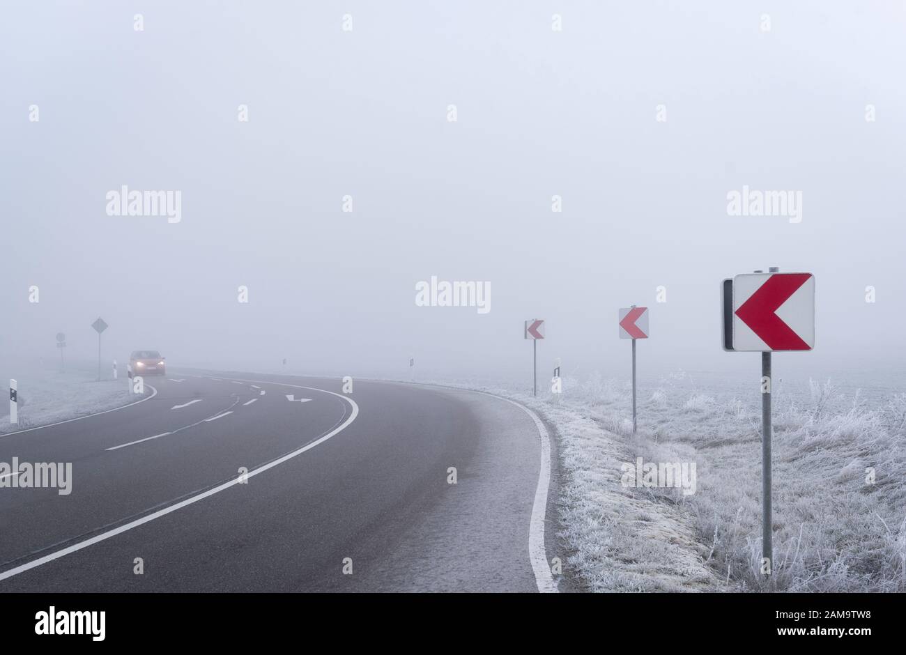 Route courbe dangereuse en hiver et panneaux d'alerte routière. Conduite par mauvais temps. Prévision de brouillard Banque D'Images