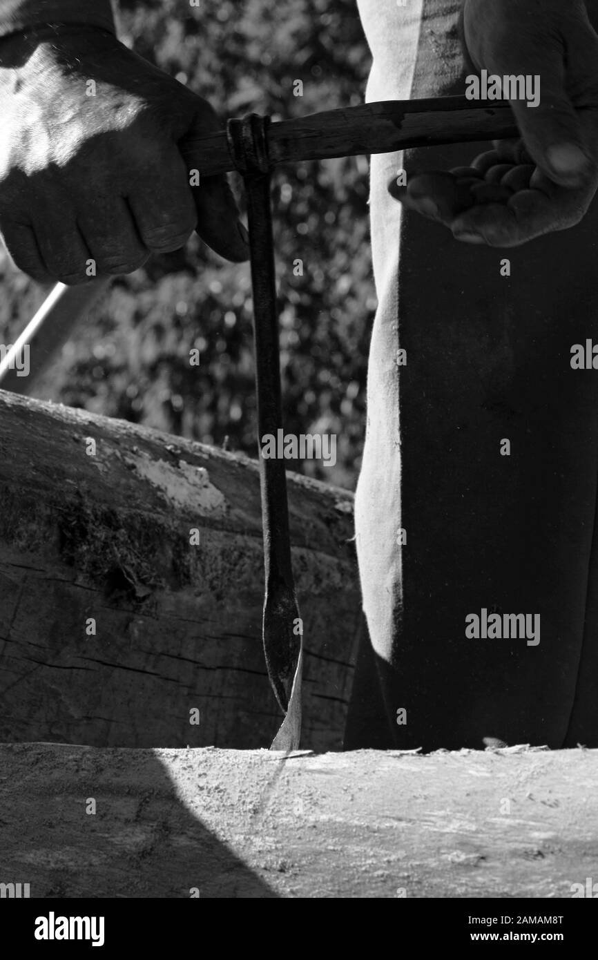 Les mains de l'homme font un trou avec une perceuse à main dans un morceau de bois. Photo en noir et blanc d'un charpentier. Banque D'Images