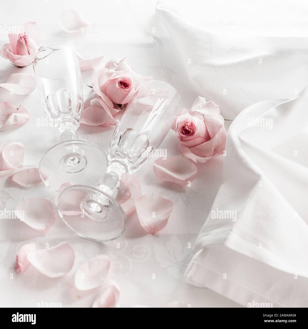 Verres à champagne en cristal de mariage sur une serviette en satin avec une bouteille de champagne et des pétales de rose Banque D'Images