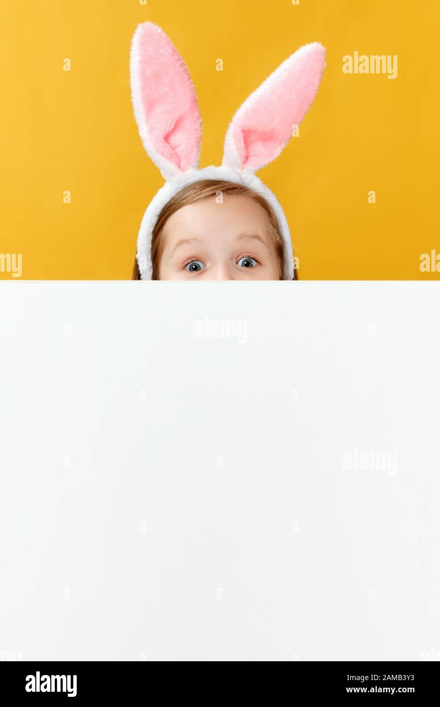 Joyeuses pâques. Drôle petite fille avec des oreilles de lapin se cache à cause d'une bannière vierge. L'enfant prése sur les œufs. Banque D'Images