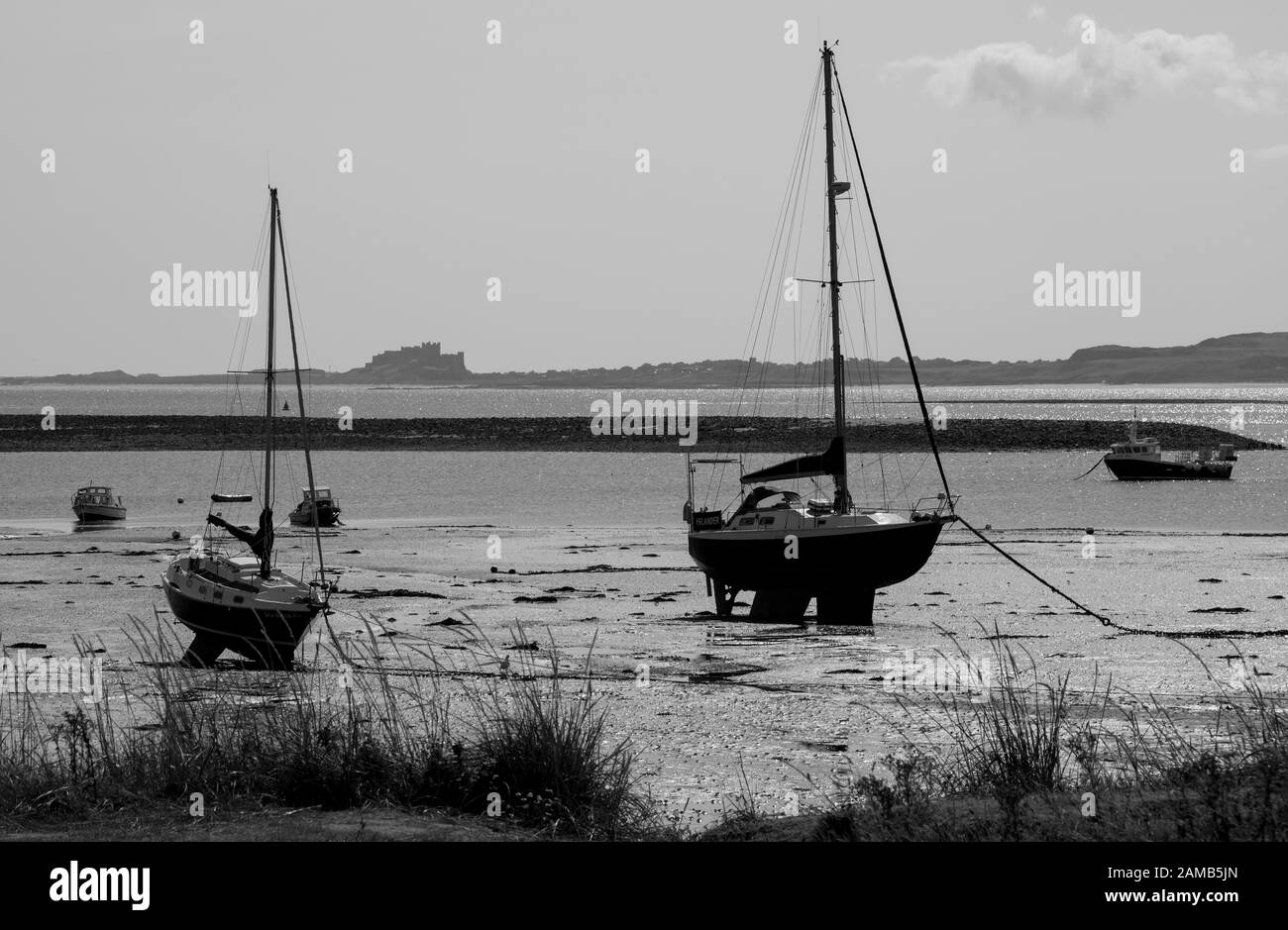 Vue de l'île Sainte en direction d'un château de Bamburgh éloigné sur la côte de Northumberland avec des yachts dans le petit port Banque D'Images