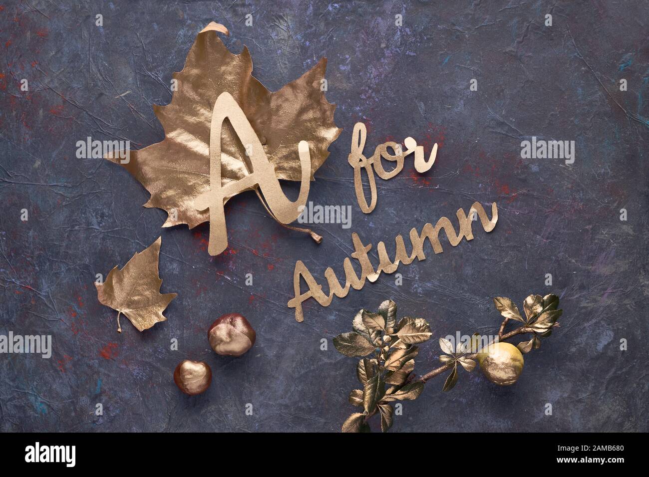 Plat d'automne avec feuilles dorées peintes et texte « A for Autumn » sur fond sombre texturé. Banque D'Images