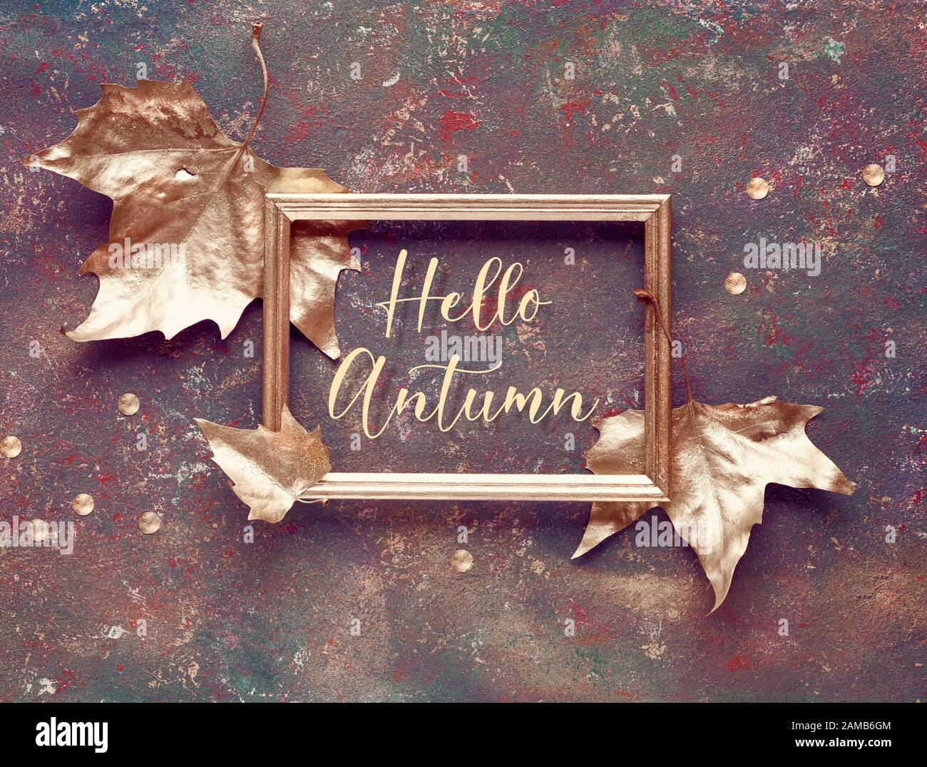 Couche plate de chute avec des feuilles de sycomore peintes en or et texte doré 'Bonjour automne' dans le cadre doré sur toile brun foncé texturé. Vue de dessus, cre décoratif Banque D'Images