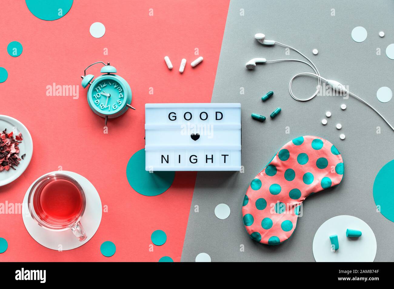 Envoyez un texte « Bonne nuit » sur la visionneuse tendance. Masque de sommeil rose avec points de polka, réveil, écouteurs et bouchons d'oreilles. Pilules, capsules et thé apaisant. Plat l Banque D'Images