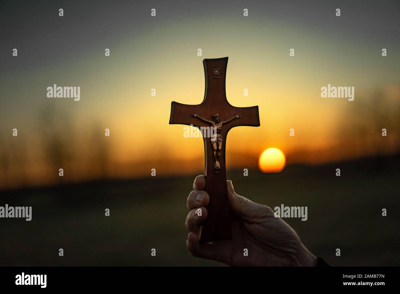 Femme priant en plein air avec un crucifix au coucher du soleil Banque D'Images