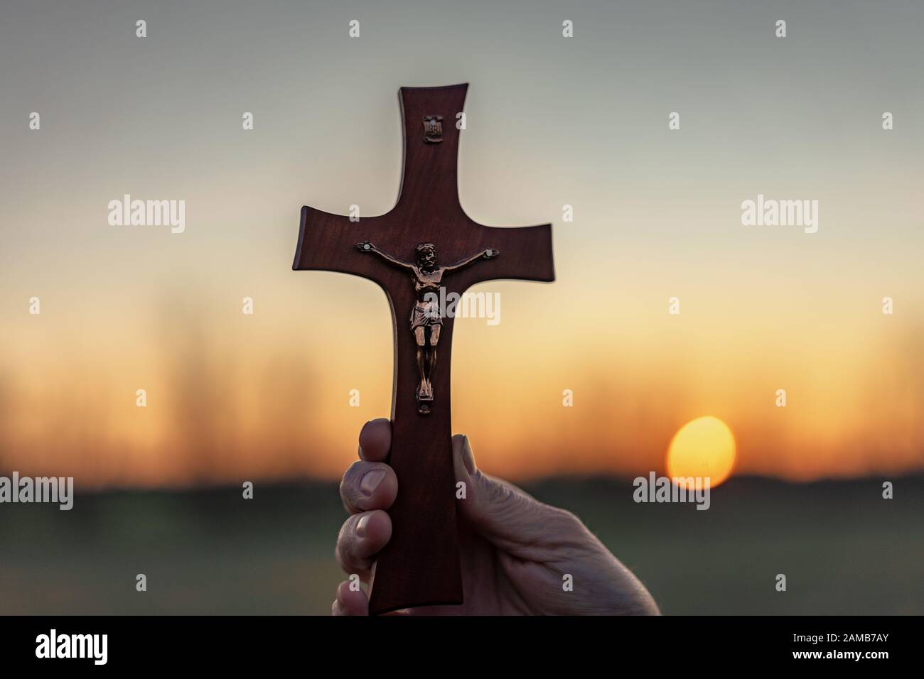 Femme priant en plein air avec un crucifix au coucher du soleil Banque D'Images