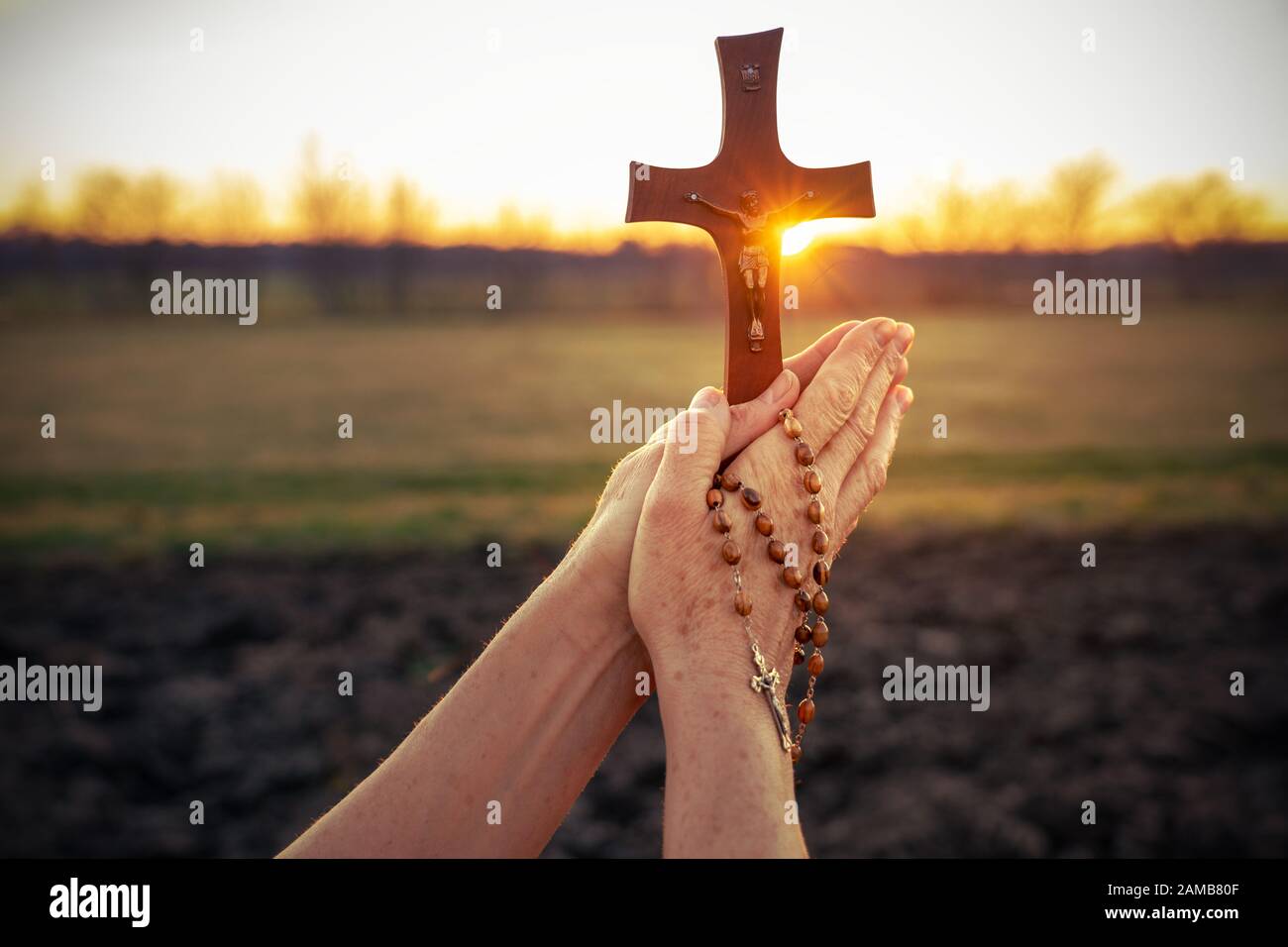 Femme priant en plein air avec un crucifix au coucher du soleil Banque D'Images