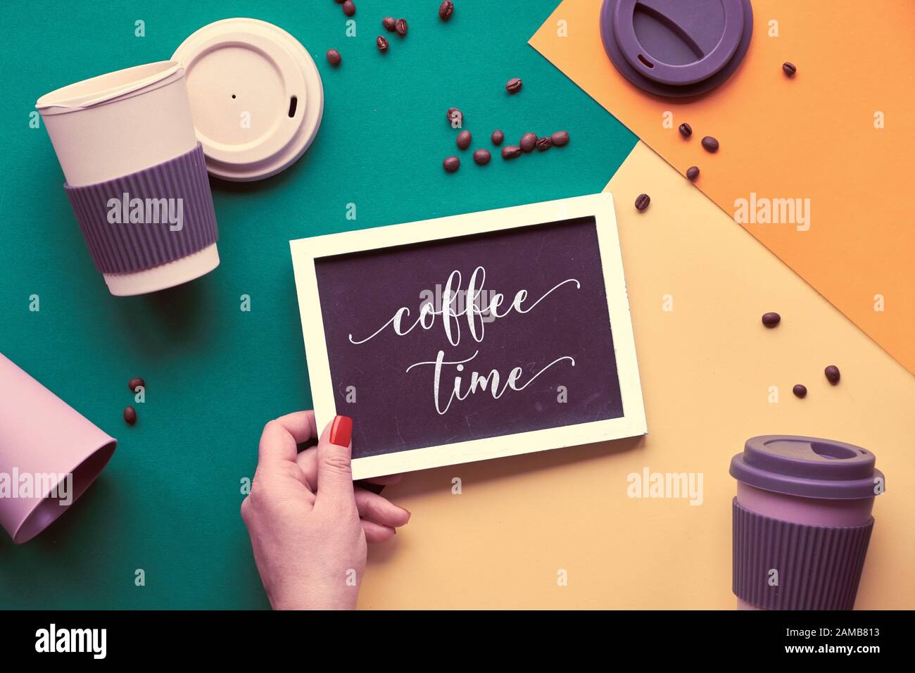 Concept de café zéro déchet. Tasses à café réutilisables écologiques dans les mains, vue géométrique du dessus sur papier fendu dans des tons vert, jaune et orange, texte Banque D'Images